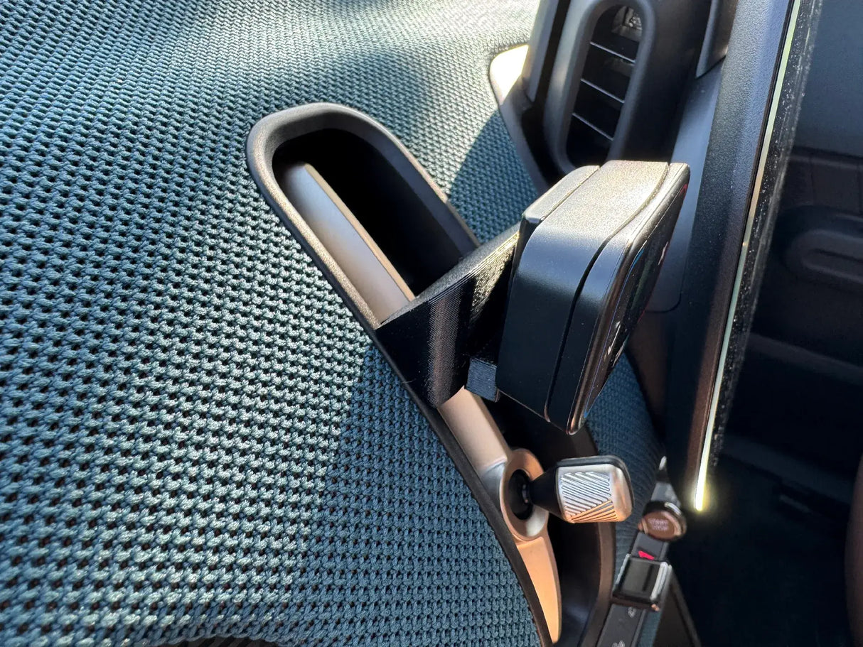 Een close-up van de Compacte Flitsmeister TWO houder voor de MINI Countryman U25 op een ventilatieklep op het dashboard, met links de gestructureerde stoelbekleding en rechts een deel van het dashboard en de ventilatiebediening van de MINI Countryman U25.