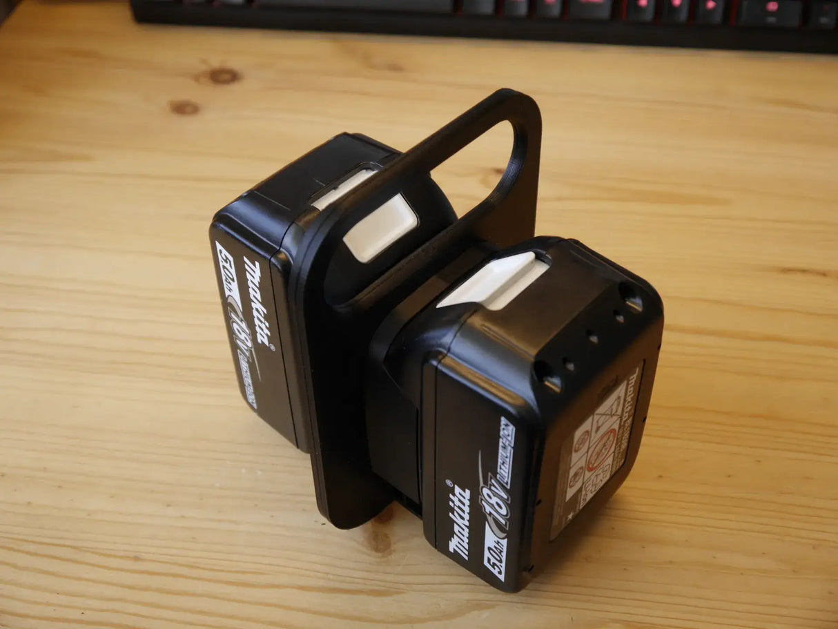 Twee zwarte Makita 18V lithium-ion accu's zijn bevestigd aan een Makita LXT 18V BL1830-BL1890 Accuhouder & Transportwagen | 3D Geprint, geplaatst op hout met een toetsenbord op de achtergrond.