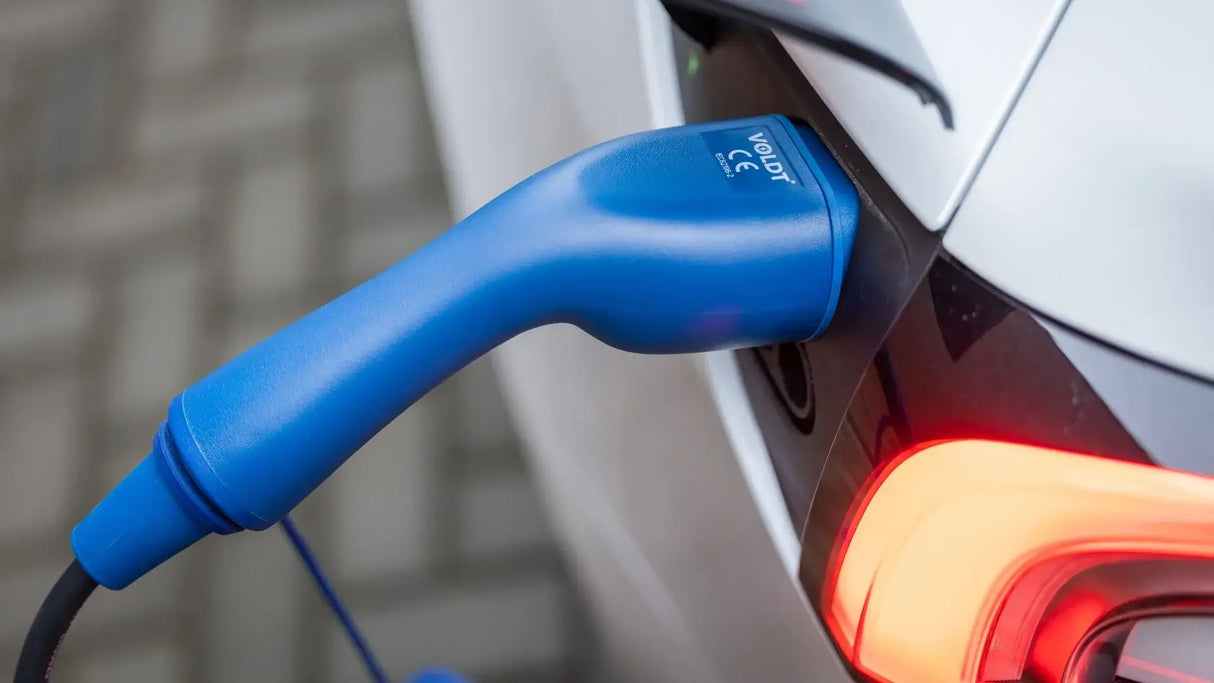 Een 🇳🇱 Type 2 Schuko 230V Mobiele laadkabel | thuislader | Regelbaar 3,7kW is aangesloten op de laadpoort van een witte elektrische auto met het achterlicht aan. De achtergrond toont een wazig oppervlak met een patroon.