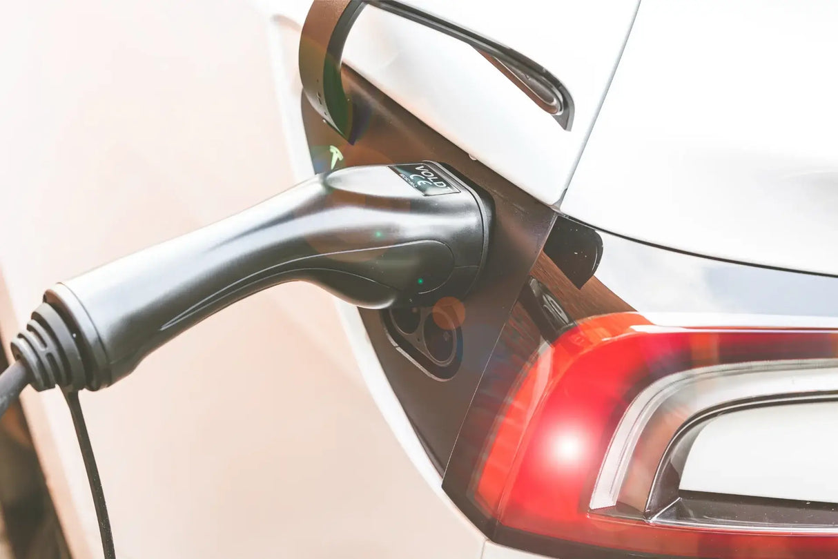 Close-up van een witte EV die wordt opgeladen met de 🇳🇱 VOLDT Booster EV Set 3-Fase 16A 11kW thuislader met multi-adapters, aangesloten op de poort van de auto in de buurt van het achterlicht. Inclusief 3 jaar garantie.