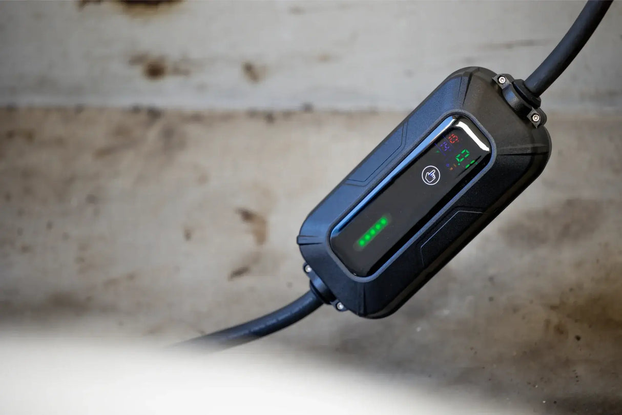 Een close-up van de VOLDT Booster EV Set 3-Fase 16A 11kW thuislader met groene LED-verlichting en digitaal display, getoond op een betonnen oppervlak. Dit Nederlandse product wordt geleverd met multi-adapters en 3 jaar garantie.