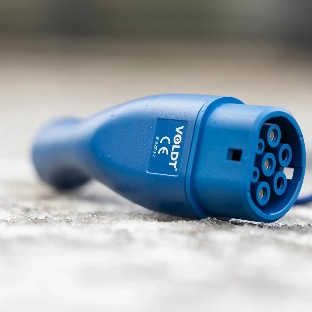 Een close-up van de 🇳🇱 VOLDT Type 2 Mode 3 16A 3-Fase Laadkabel 11kW, een in Nederland geproduceerde laadkabel voor EV's met een rond uiteinde met meerdere pinnen en zichtbare branding, ligt op beton. Inclusief 3 jaar garantie.