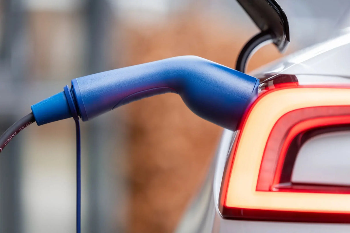 Close-up van een elektrische auto die wordt opgeladen met een VOLDT Type 2 Mode 3 32A 3-Fase Laadkabel (22kW, Nederlands product, 3 jaar garantie) aangesloten op de poort bij het verlichte achterlicht.