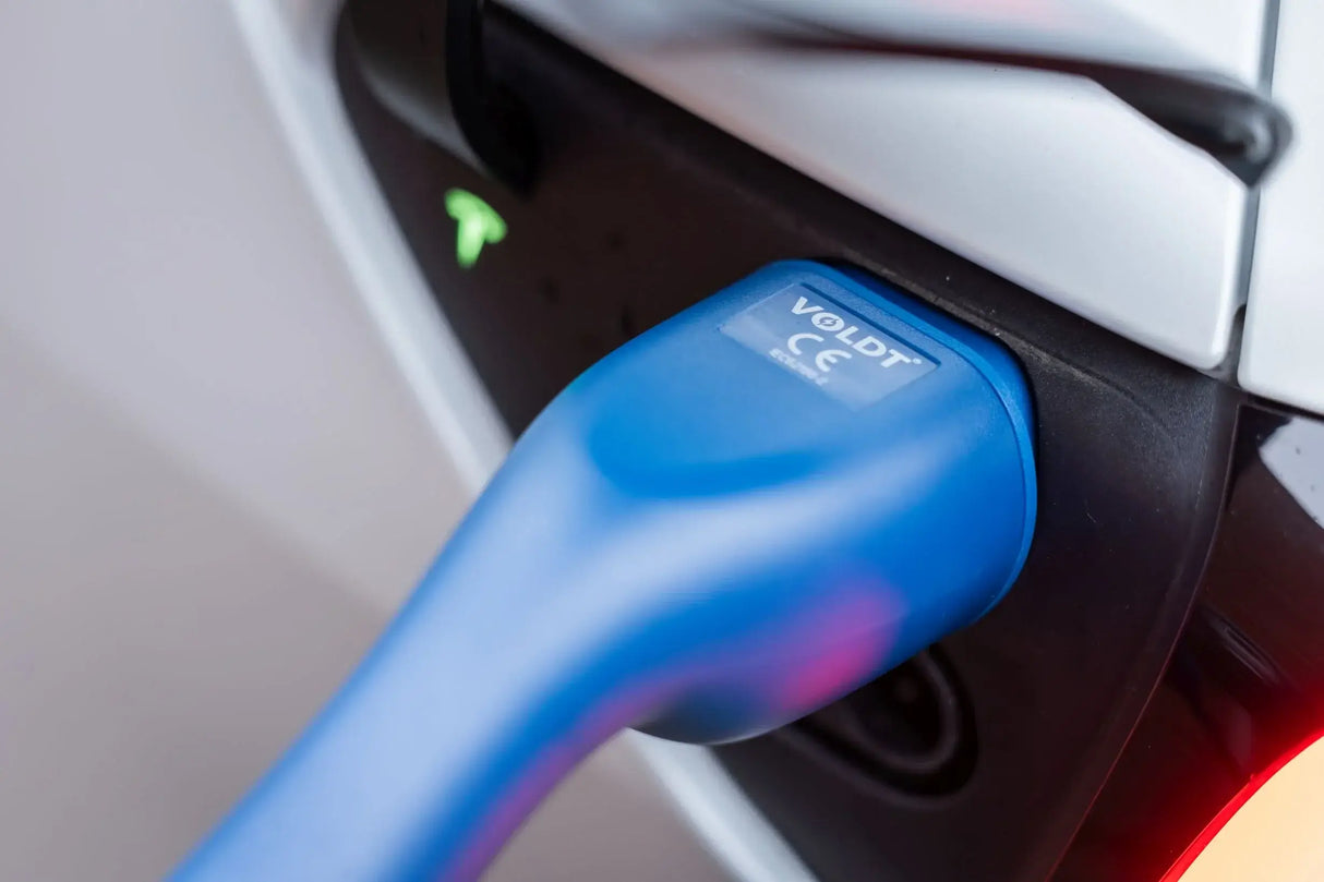 Close-up van een blauwe VOLDT Type 2 Mode 3 32A 3-Fase Laadkabel 22kW aangesloten op de laadpoort van een witte auto, met een oplichtend groen indicatielampje erboven. Gemaakt in Nederland met 3 jaar garantie.