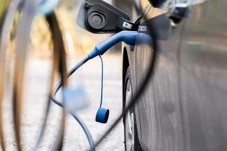 Een close-up van een zwarte elektrische auto die wordt opgeladen met de 🇳🇱 VOLDT Type 2 Mode 3 32A 3-Fase Laadkabel 22kW, een Nederlands product met een blauwe kabel en 3 jaar garantie, aangesloten op de poort van de auto en een weerspiegeling van de omgeving.