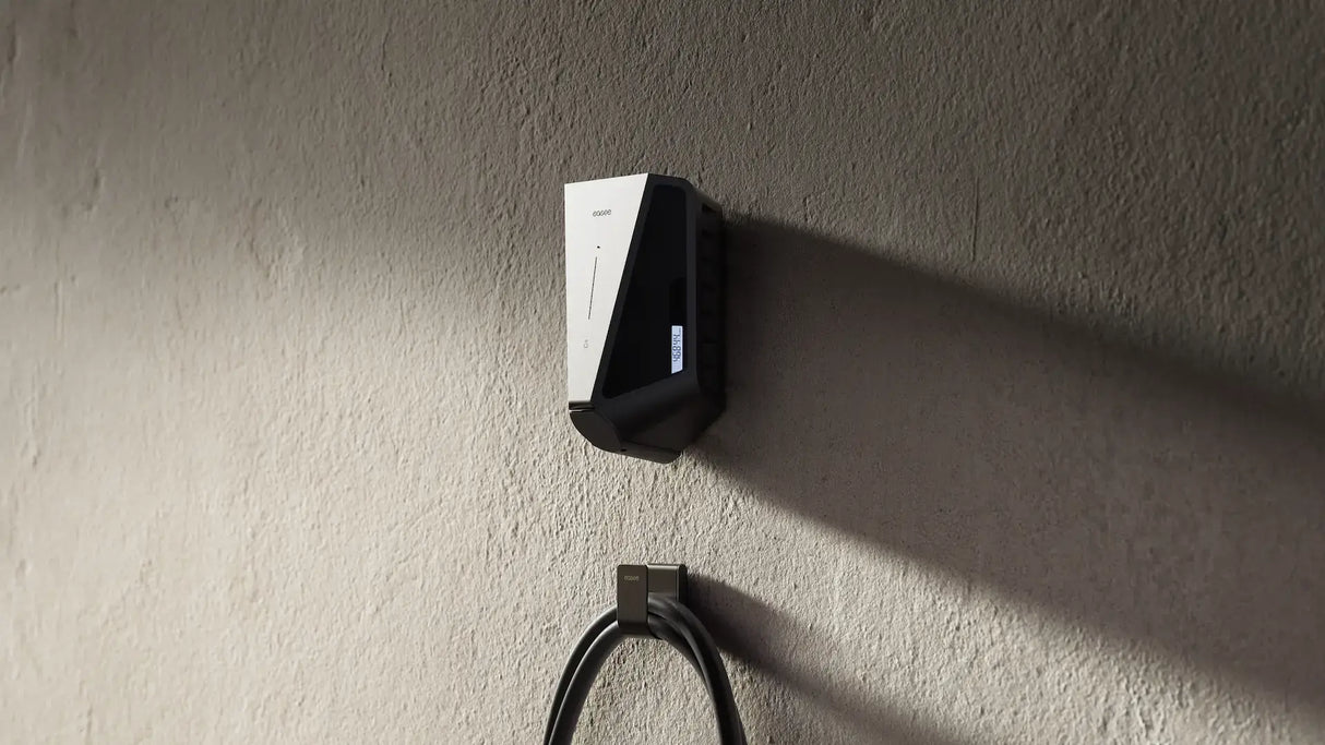Een Easee Charge Max 22kW oplaadpunt elektrisch voertuig in zwart-wit is wandgemonteerd op een beige muur, met de laadkabel eronder-ideaal voor efficiënte laadpaal thuis installatie.