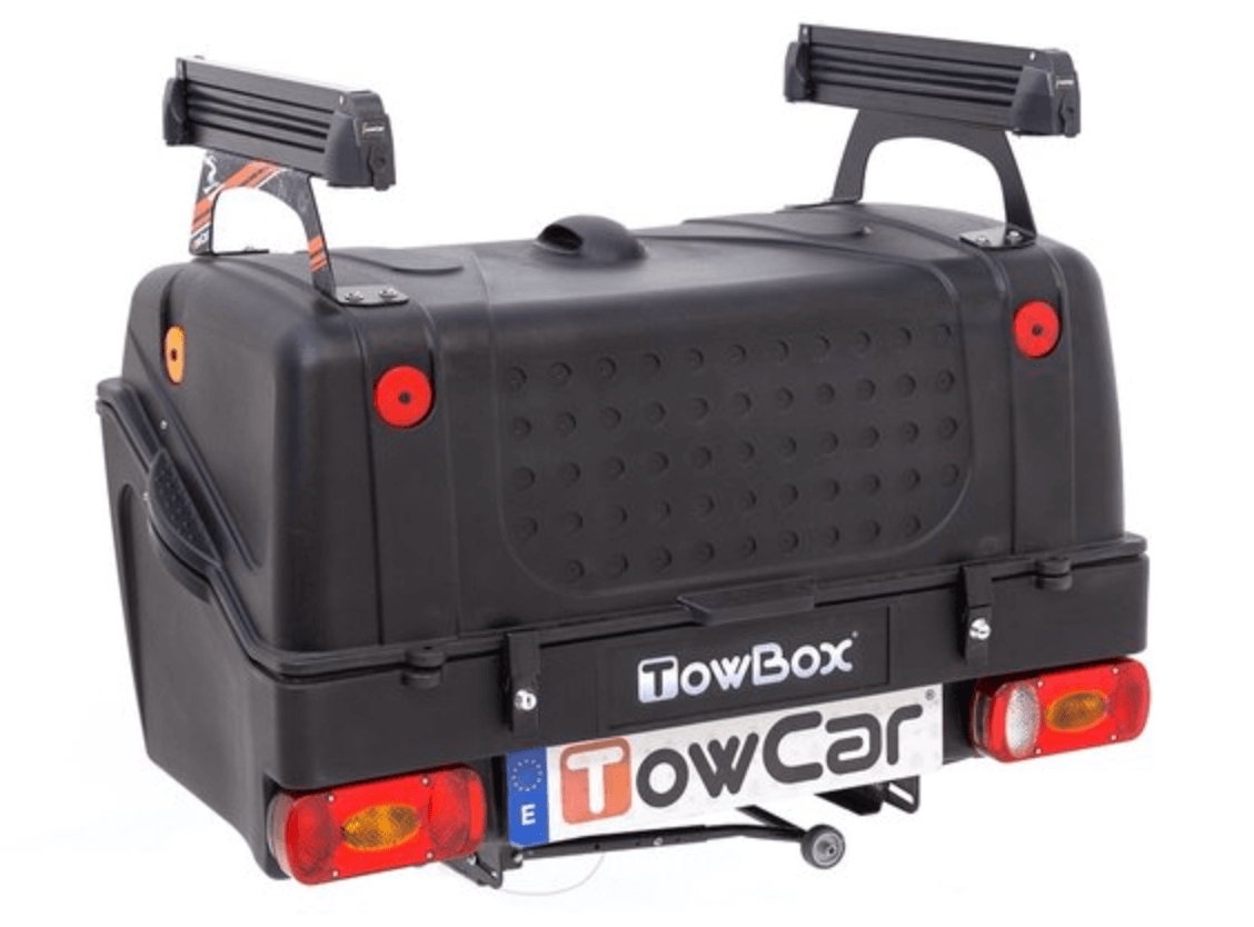 Te huur: Towbox V1 met skidragers - ook ideaal voor wintersport. De stevige zwarte bagagebox heeft achterlichten, een TowCar-kentekenplaat en afgeronde hoeken - perfect voor avonturen met je elektrische auto!.