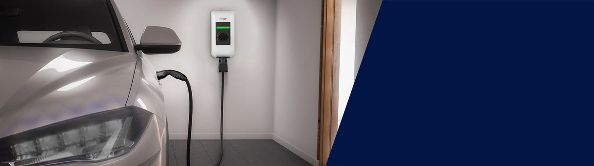 Een zilverkleurige elektrische auto staat geparkeerd in een garage, aangesloten op een Laadstation SolarEdge Home EV 22kW Type 2 met 6 meter kabel, met een wit design en groen indicatielampje - perfect voor efficiënt zonne-energie laden.
