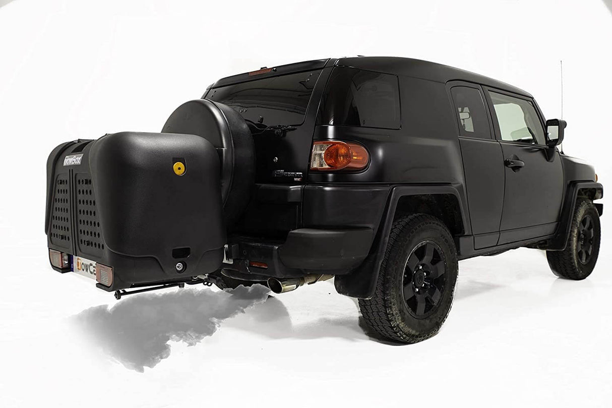 Een zwarte SUV met off-road banden wordt getoond vanaf de achterkant, met een Te huur: Bagagebox trekhaakbox Trekhaakbox V2 390 liter en een reservewiel gemonteerd op de achterkant, tegen een effen witte achtergrond.