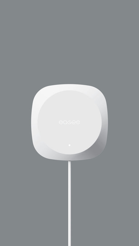 Een witte, vierkante Easee Equalizer Load balancing voor P1 poort van slimme meter met afgeronde hoeken en "easee" erop is gemonteerd op een grijze muur. Eronder hangt een witte kabel - perfect voor laadpaal thuis en slim opladen in je huisinstallatie.