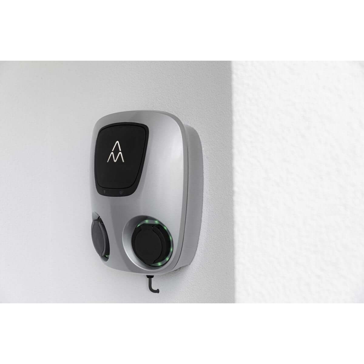 Een Charge Amps Aura laadstation met Sim 2x22 kW 3-fase 32A bidirectioneel vehicle to grid, zilverkleurig en wandgemonteerd, met twee ronde poorten en verlichte indicator. Ideaal voor het efficiënt laden van elektrische auto's.