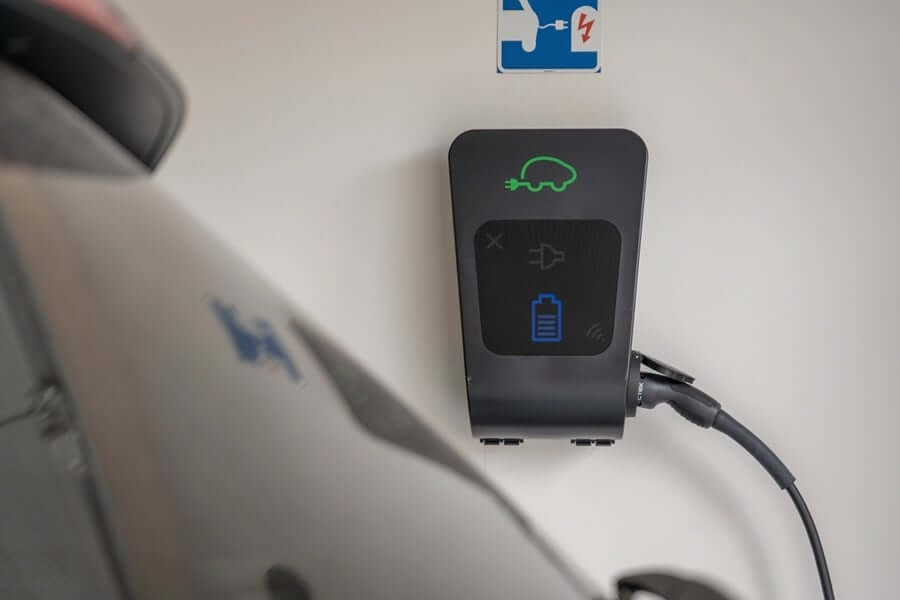 De CTEK Chargestorm Connected 2 11kW/22kW laadpaal voor elektrische auto's is een aan de muur bevestigd EV-laadstation met een aangesloten auto, waarop pictogrammen voor auto, accu en stekker worden weergegeven om de laadstatus en ondersteuning voor load balancing aan te geven.