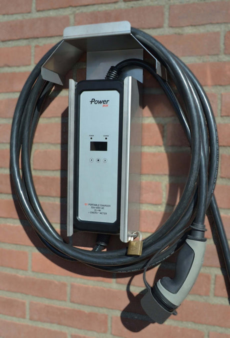 De Thuislader voor stopcontact Ratio Power Box 3-Fase 16A/32A met een 5-meter Type 2 opgerolde zwarte kabel is aan de muur gemonteerd op een bakstenen muur in fel zonlicht.
