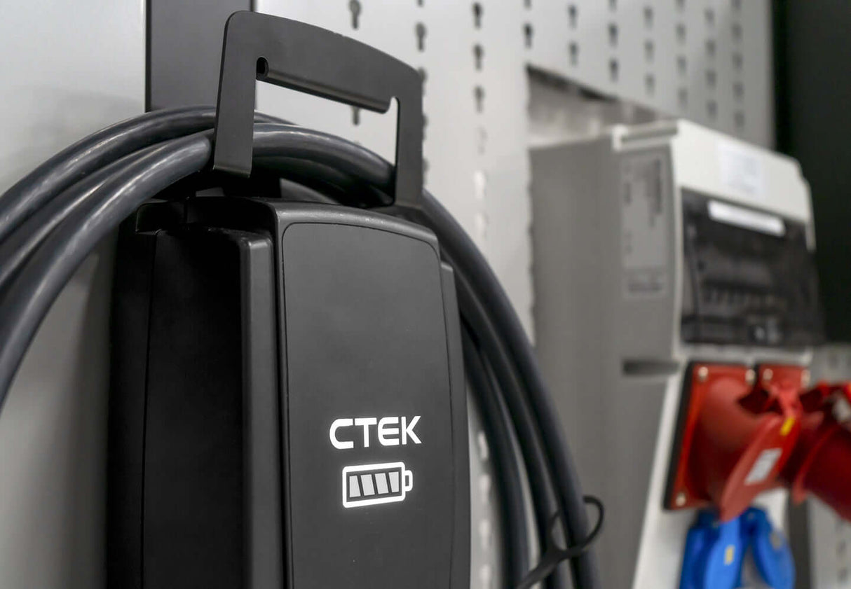 De CTEK NJORD GO 3x16A 11kW thuislader met 6,5 meter kabel wordt aan de muur bevestigd in de buurt van stopcontacten en een elektriciteitskast en biedt een efficiënte thuislaadoplossing voor uw garage of werkplaats.