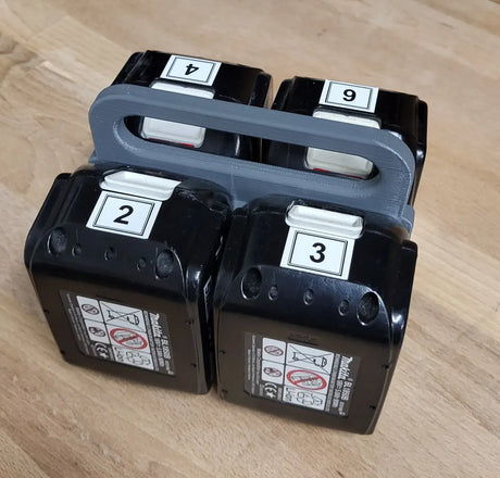 Vier zwarte Makita accu's met de labels 2, 3, 4 en 6 liggen in een Makita Accuhouder & Transport Drager | 3D geprint | Zwart op een houten oppervlak.