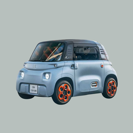 Een kleine, lichtblauwe elektrische auto met oranje velgen en een compact ontwerp, gezien vanaf de linker voorkant tegen een effen grijze achtergrond.