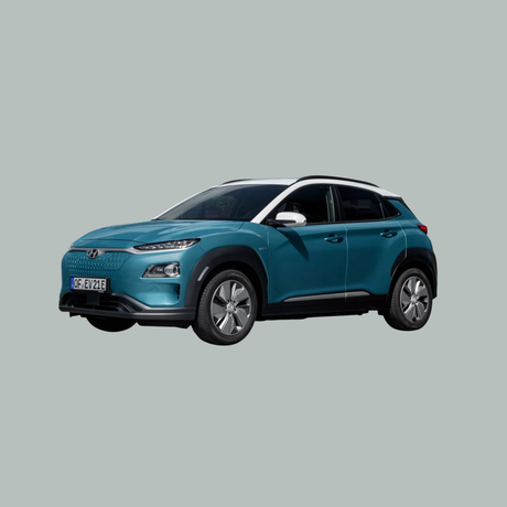 Een groenblauwe Hyundai Kona elektrische SUV staat geparkeerd op een effen grijze achtergrond, schuin geplaatst om de voor- en linkerkant te laten zien. De auto heeft zilveren sierstrips, opvallende koplampen en aerodynamische wielen.