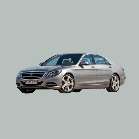 Een zilverkleurige luxe sedan, waarschijnlijk een Mercedes-Benz, staat geparkeerd op een effen lichtgrijze achtergrond, schuin geplaatst om de voor- en zijkant van de auto te laten zien.