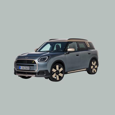 Een lichtgrijze Mini Cooper SUV met zwarte en beige accenten staat geparkeerd op een effen lichtgrijze achtergrond, iets naar links gericht.