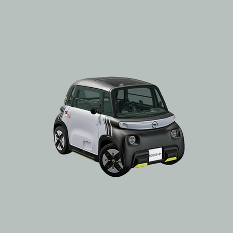 Een compacte, tweedeurs elektrische auto met een grijze en zwarte carrosserie, afgeronde hoeken en unieke gestreepte details op de zijkant, tegen een effen lichtgrijze achtergrond.