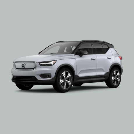 Een witte Volvo XC40 elektrische SUV staat geparkeerd op een effen lichtgrijze achtergrond, gezien vanaf de linkervoorkant. Het moderne design, het zwarte dak en de lichtmetalen velgen komen goed tot hun recht.