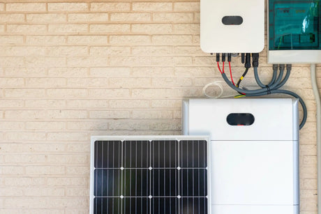 Zonnepaneel en elektrische apparatuur geïnstalleerd op een lichtgekleurde bakstenen muur, inclusief kabels, een regelkast en een batterijopslag voor zonne-energie.
