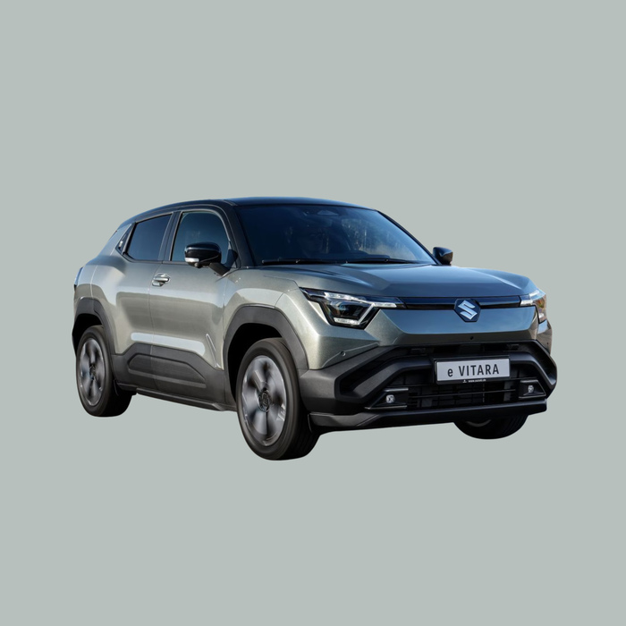 Een zilverkleurige Suzuki e-Vitara elektrische SUV is afgebeeld op een effen, lichtgrijze achtergrond, gezien vanuit de hoek linksvoor. De auto heeft scherpe lijnen, opvallende koplampen en moderne designelementen.