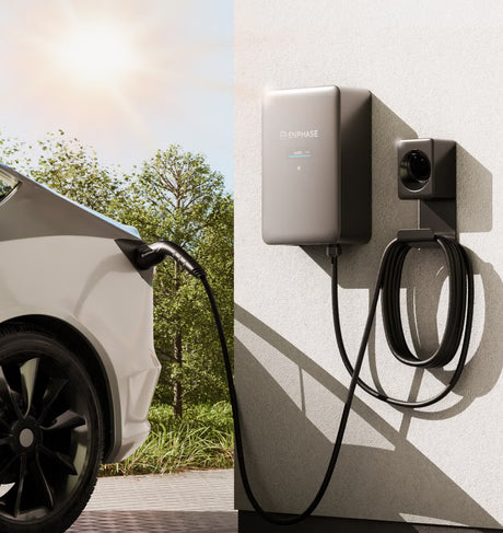 Een witte elektrische auto wordt buiten opgeladen, aangesloten op een aan de muur gemonteerde Enphase IQ EV Charger 2 | 22 kW – 3-fasig – Type 2-aansluiting met MID & AI-beheer, met behulp van een zwarte spiraalkabel. Bomen benadrukken het milieuvriendelijke opladen met deze geavanceerde laadpaal.
