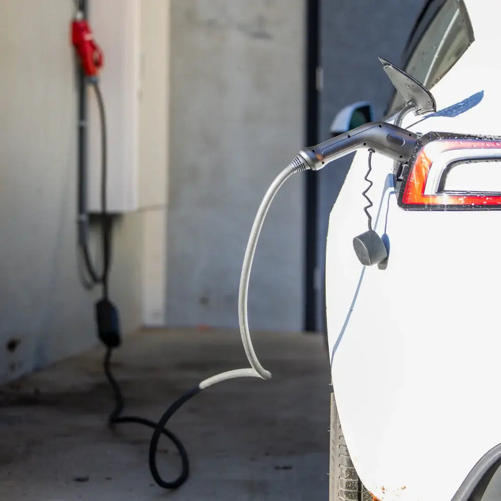 Een close-up van een elektrische auto die wordt opgeladen met de Type 2 CEE 32A 3-Fase Mobiele Laadkabel Verstelbaar 22kW, een in Nederland geproduceerde verstelbare kabel (3 jaar garantie), ingeplugd bij een gebouw met de wandlader.
