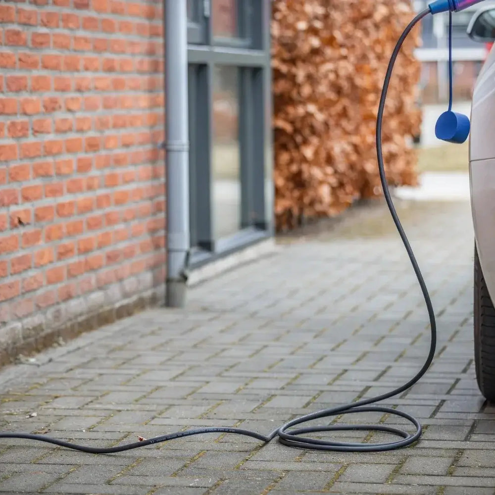 Een zilverkleurige elektrische auto staat geparkeerd op een oprit en wordt opgeladen met de 🇳🇱 Type 2 Schuko 230V Mobiele laadkabel | thuislader | Regelbaar 3,7kW | 3 jaar garantie. Dit laat zien hoe handig thuis EV opladen is met dit Nederlandse product.
