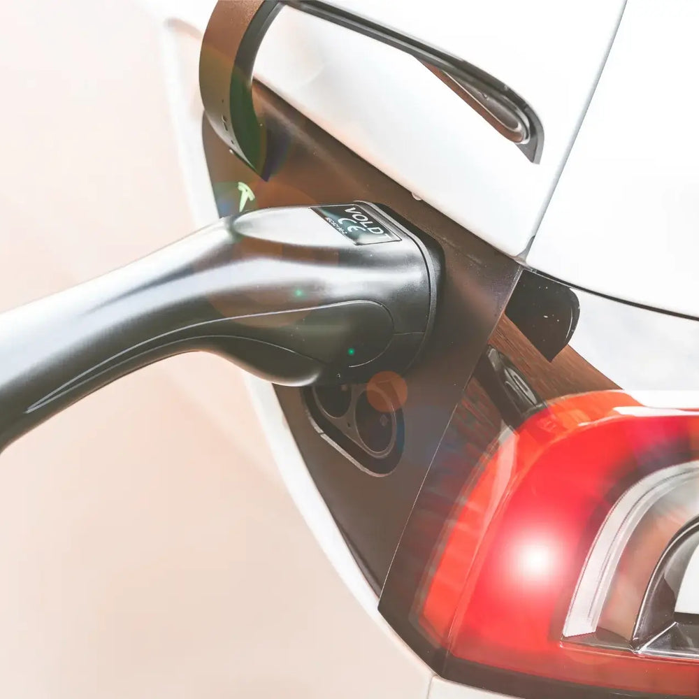 Close-up van een witte EV die wordt opgeladen met de 🇳🇱 VOLDT Booster EV Set 3-Fase 16A 11kW thuislader met multi-adapters, aangesloten op de poort van de auto in de buurt van het achterlicht. Inclusief 3 jaar garantie.