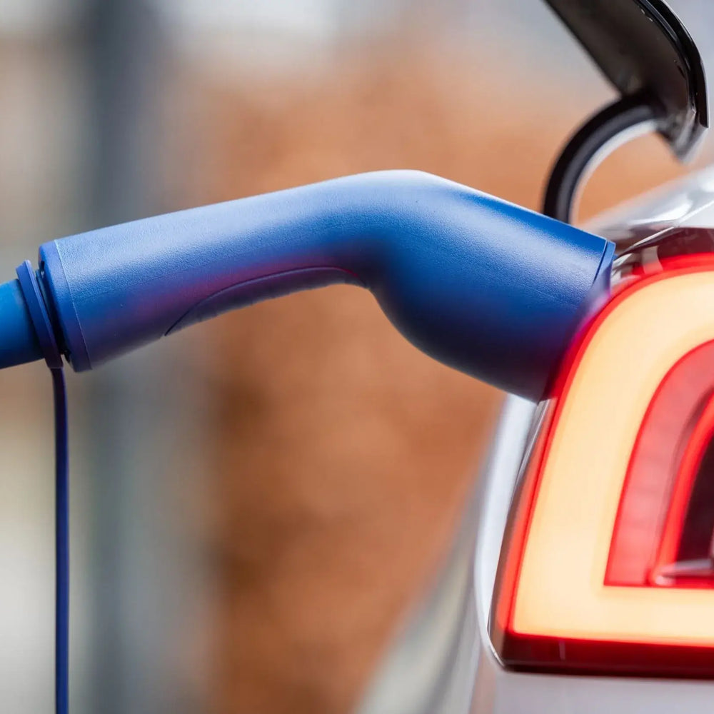 Close-up van een elektrische auto die wordt opgeladen met een VOLDT Type 2 Mode 3 32A 3-Fase Laadkabel (22kW, Nederlands product, 3 jaar garantie) aangesloten op de poort bij het verlichte achterlicht.