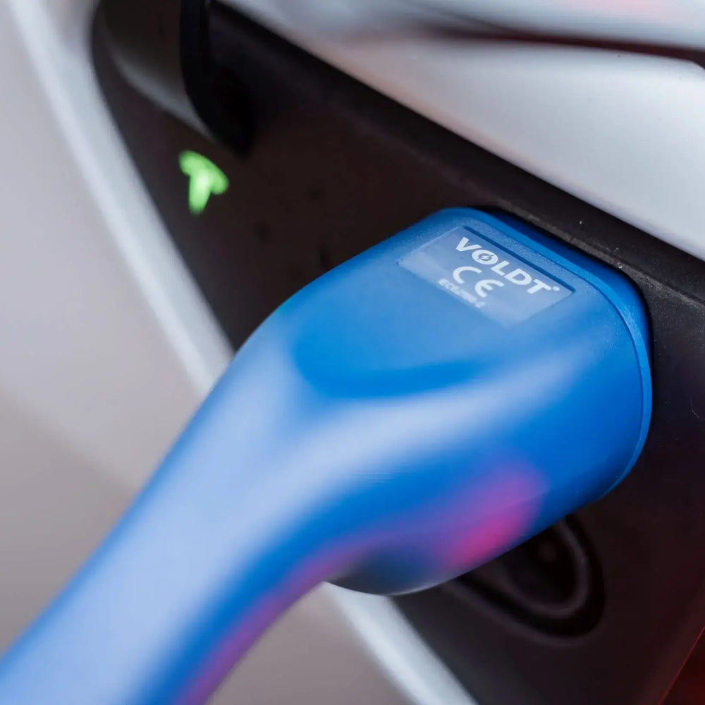 Close-up van een blauwe VOLDT Type 2 Mode 3 32A 3-Fase Laadkabel 22kW aangesloten op de laadpoort van een witte auto, met een oplichtend groen indicatielampje erboven. Gemaakt in Nederland met 3 jaar garantie.
