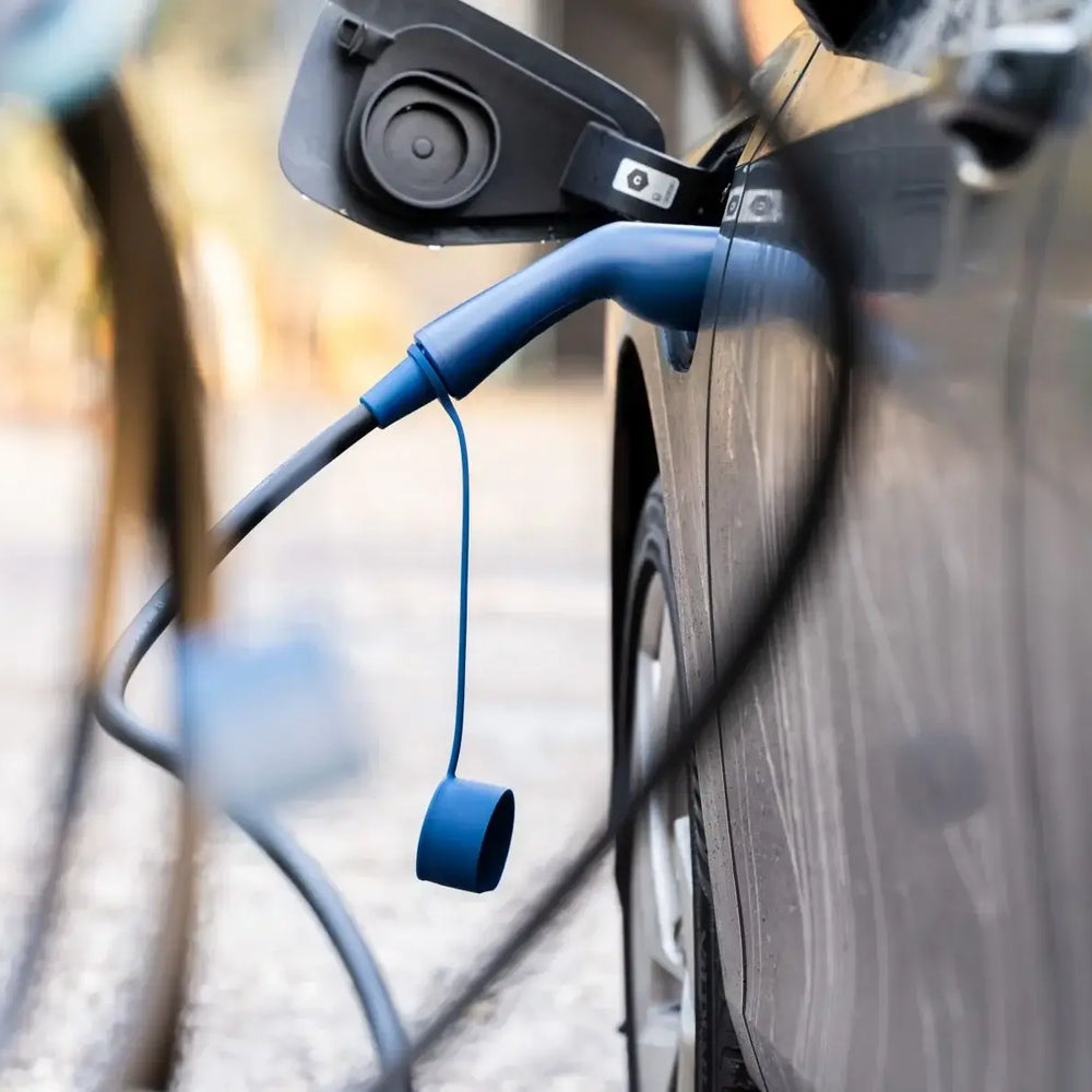 Een close-up van een zwarte elektrische auto die wordt opgeladen met de 🇳🇱 VOLDT Type 2 Mode 3 32A 3-Fase Laadkabel 22kW, een Nederlands product met een blauwe kabel en 3 jaar garantie, aangesloten op de poort van de auto en een weerspiegeling van de omgeving.