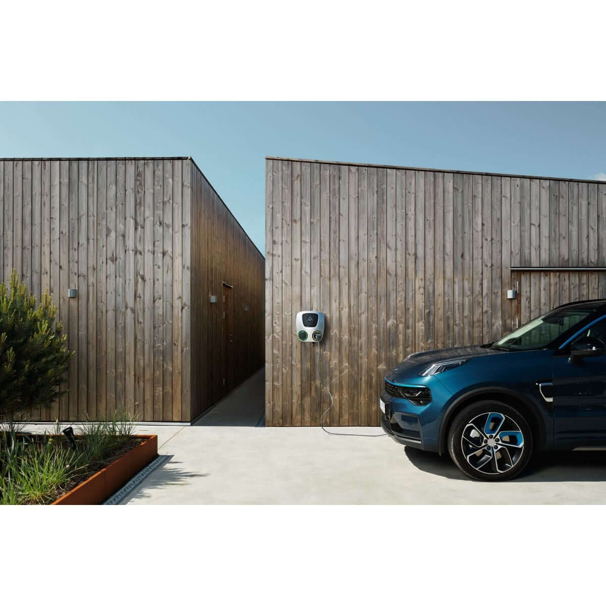 Een blauwe elektrische auto laadt op bij een Laadstation Charge Amps Aura met Sim 2x22 kW 3-fase 32A bi-directioneel vehicle to grid, gemonteerd aan de houten gevel van een modern gebouw op een zonnige dag.