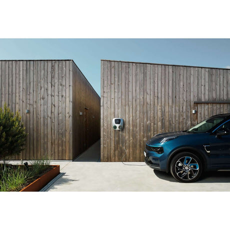 Een blauwe elektrische auto laadt op bij een Laadstation Charge Amps Aura met Sim 2x22 kW 3-fase 32A bi-directioneel vehicle to grid, gemonteerd aan de houten gevel van een modern gebouw op een zonnige dag.
