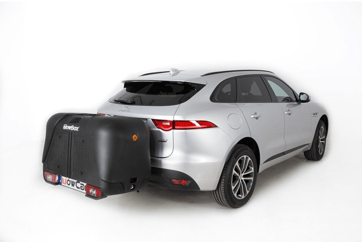 Een zilveren SUV op een witte achtergrond met een grote zwarte Te huur: Bagagebox trekhaakbox Trekhaakbox V2 390 liter bevestigd aan de achterkant, die de kentekenplaat bedekt en enkele meters achter het voertuig uitsteekt.