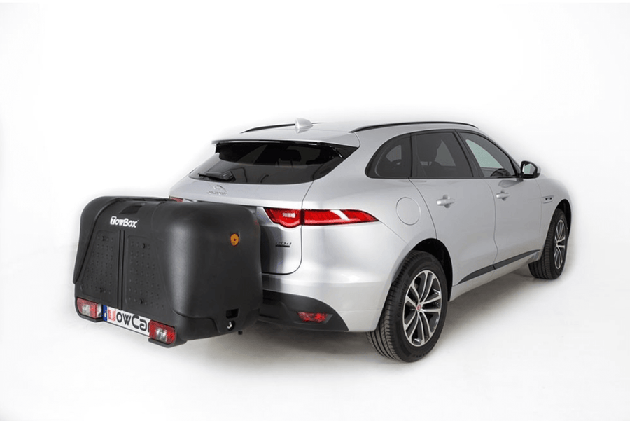 Een zilveren SUV op een witte achtergrond met een grote zwarte Te huur: Bagagebox trekhaakbox Trekhaakbox V2 390 liter bevestigd aan de achterkant, die de kentekenplaat bedekt en enkele meters achter het voertuig uitsteekt.